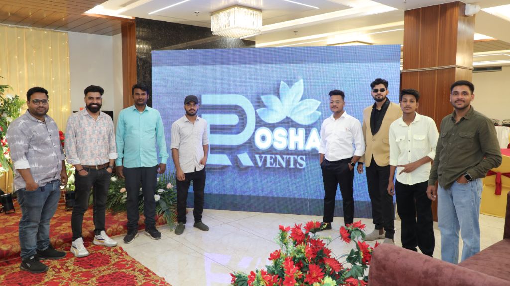 Roshan Events Team standing in front of the Roshan Events LED display at an event venue